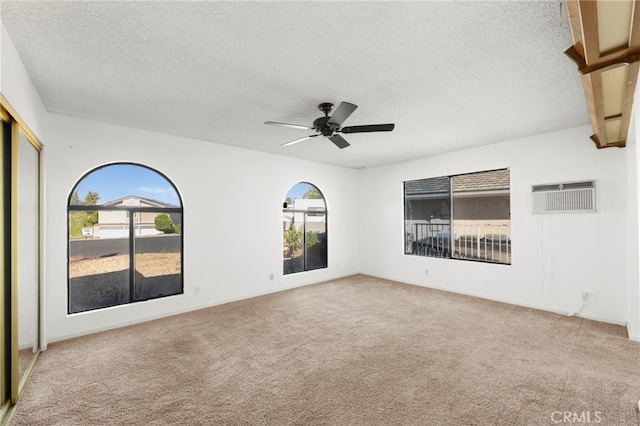 carpeted empty room with a textured ceiling, a wall unit AC, and a ceiling fan