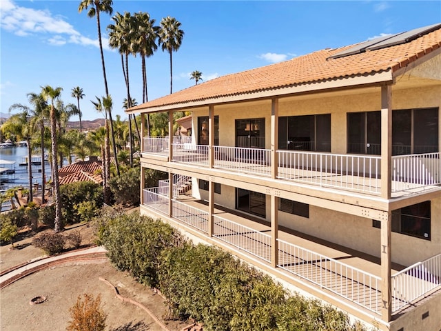 view of side of property with a balcony, a tiled roof, a water view, a patio area, and stucco siding