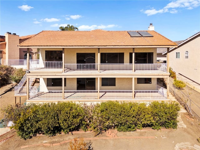 view of front of home with a chimney, stucco siding, roof mounted solar panels, a balcony, and a tiled roof