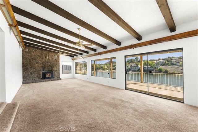 unfurnished living room featuring lofted ceiling with beams, ceiling fan, a stone fireplace, a textured ceiling, and carpet flooring