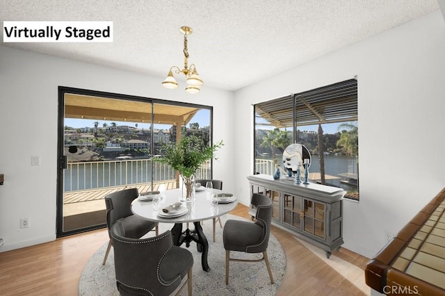 dining area with a textured ceiling, a water view, wood finished floors, and a notable chandelier