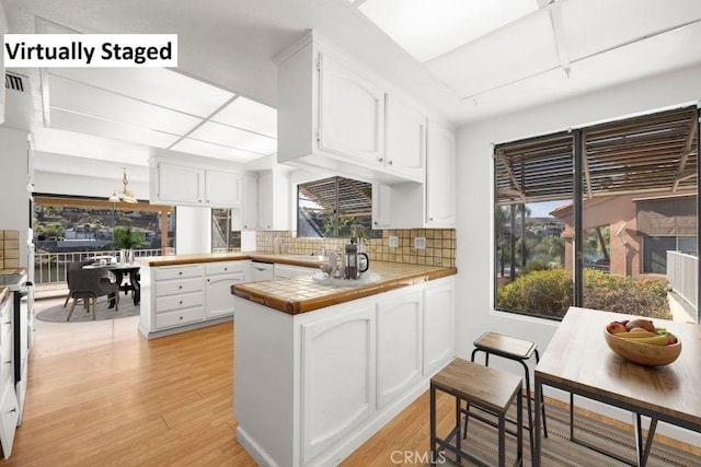 kitchen featuring tile counters, white cabinets, a peninsula, light wood-type flooring, and backsplash