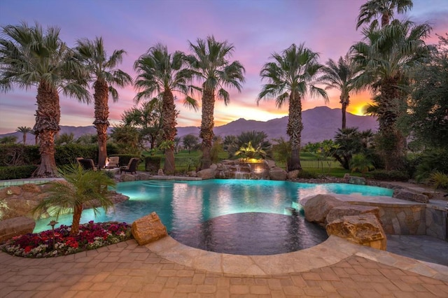 pool at dusk featuring a mountain view, an in ground hot tub, and a patio