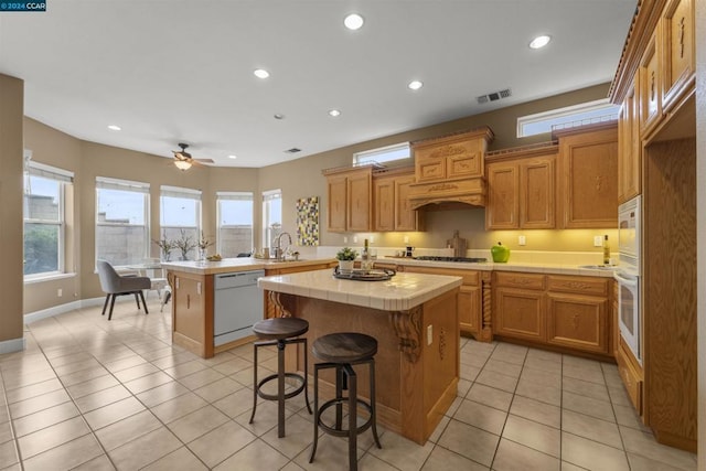 kitchen with white appliances, ceiling fan, a kitchen island, tile counters, and light tile patterned flooring