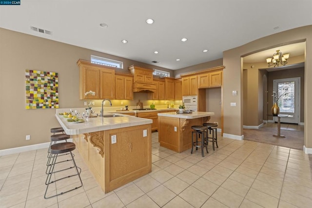 kitchen featuring sink, gas stovetop, kitchen peninsula, a kitchen bar, and light tile patterned flooring