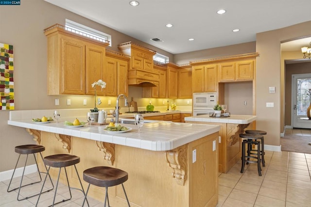 kitchen featuring white appliances, light tile patterned floors, tile counters, kitchen peninsula, and a breakfast bar area