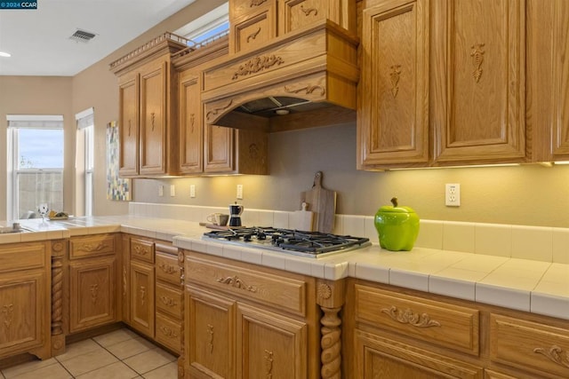 kitchen with stainless steel gas stovetop, tile counters, custom range hood, and light tile patterned floors