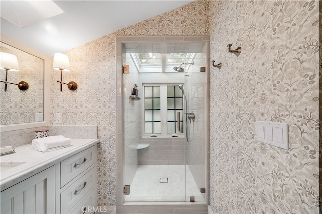 bathroom featuring lofted ceiling, wallpapered walls, a shower stall, and vanity