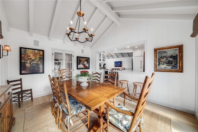 dining room with vaulted ceiling with beams, light wood-style floors, a decorative wall, and an inviting chandelier