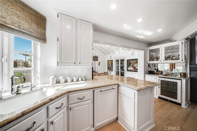 kitchen with glass insert cabinets, white cabinetry, a sink, and a peninsula