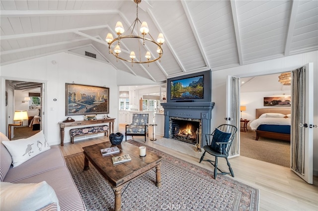 living room featuring a warm lit fireplace, visible vents, lofted ceiling with beams, an inviting chandelier, and light wood-type flooring