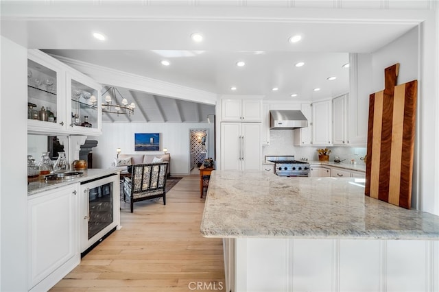 kitchen featuring high end stove, wall chimney exhaust hood, light stone counters, and white cabinets