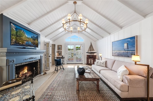 living area featuring french doors, a notable chandelier, lofted ceiling with beams, wood finished floors, and a warm lit fireplace