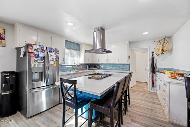 kitchen with island exhaust hood, appliances with stainless steel finishes, white cabinets, and light hardwood / wood-style flooring