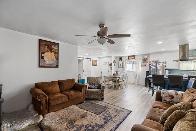 living room featuring ceiling fan, a barn door, and light hardwood / wood-style flooring