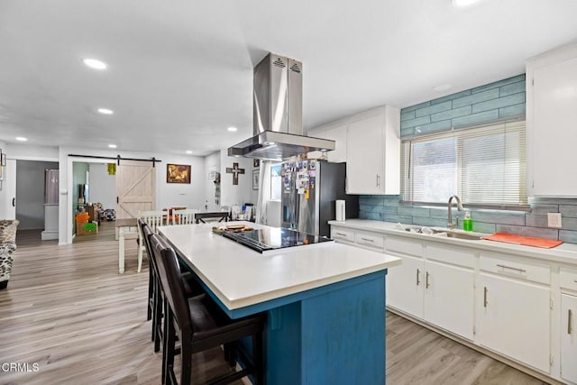 kitchen with island range hood, sink, a barn door, white cabinets, and a kitchen island