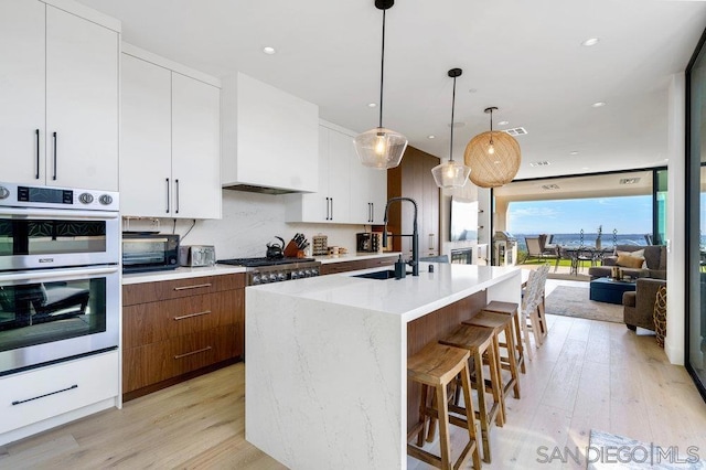 kitchen featuring sink, stainless steel appliances, an island with sink, white cabinets, and decorative light fixtures