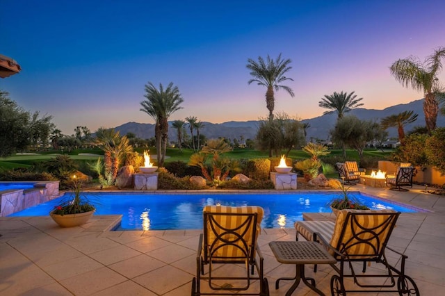 pool at dusk featuring a mountain view, a patio area, an outdoor fire pit, and a jacuzzi