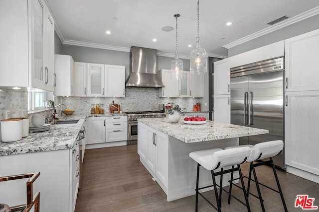 kitchen featuring a center island, high end appliances, white cabinets, wall chimney range hood, and sink