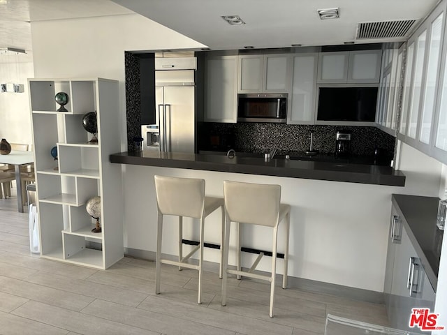 kitchen with light hardwood / wood-style flooring, backsplash, kitchen peninsula, a kitchen bar, and appliances with stainless steel finishes