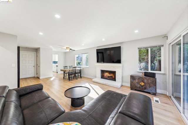 living room with ceiling fan, plenty of natural light, light hardwood / wood-style floors, and a brick fireplace