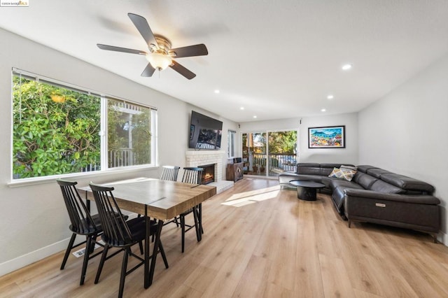 dining space with a fireplace, ceiling fan, and light wood-type flooring