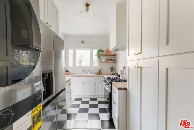 kitchen with decorative backsplash, stainless steel appliances, sink, butcher block countertops, and white cabinetry