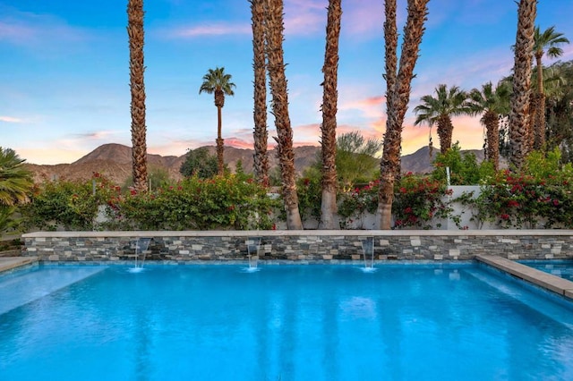 pool at dusk featuring pool water feature and a mountain view