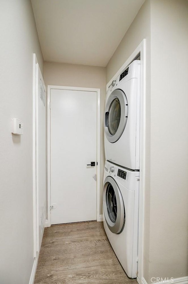 laundry room featuring stacked washer / drying machine and light wood-type flooring