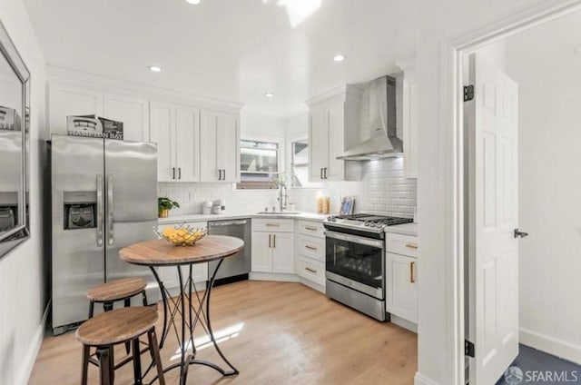 kitchen featuring light hardwood / wood-style floors, appliances with stainless steel finishes, wall chimney exhaust hood, white cabinets, and sink