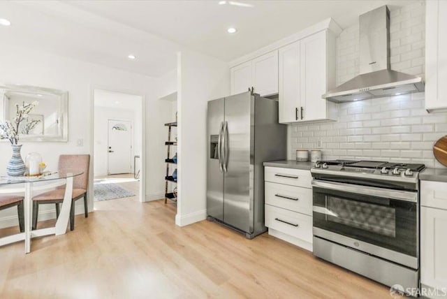 kitchen featuring white cabinets, wall chimney exhaust hood, stainless steel appliances, light hardwood / wood-style floors, and backsplash