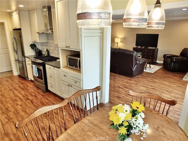 kitchen featuring wall chimney exhaust hood, stainless steel appliances, tasteful backsplash, pendant lighting, and wood-type flooring