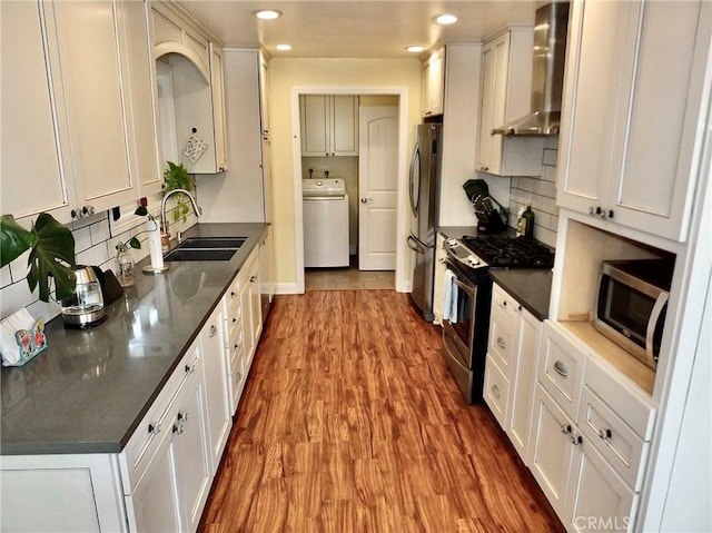 kitchen featuring appliances with stainless steel finishes, white cabinetry, washer / dryer, and wall chimney range hood