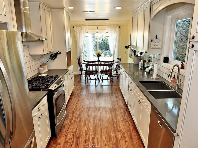 kitchen with decorative backsplash, appliances with stainless steel finishes, sink, wood-type flooring, and hanging light fixtures