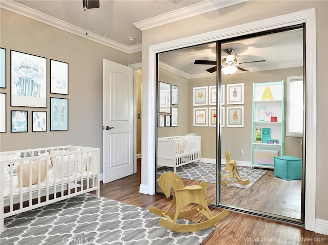 bedroom featuring a crib, hardwood / wood-style flooring, ceiling fan, and ornamental molding