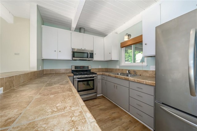 kitchen with white cabinets, tile counters, stainless steel appliances, and light hardwood / wood-style flooring