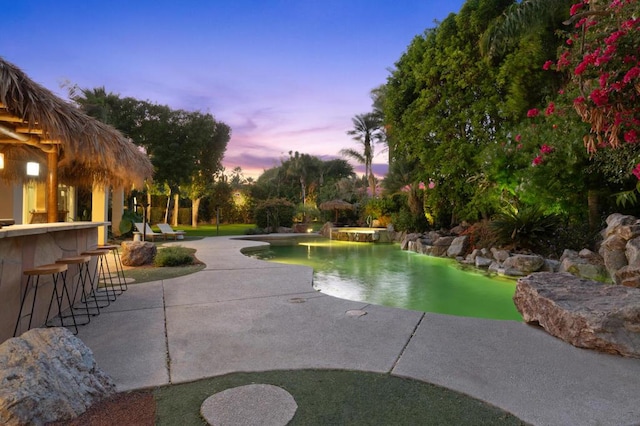 pool at dusk featuring a patio area and a bar