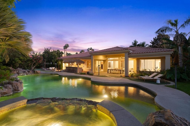 pool at dusk with a patio area, ceiling fan, and an in ground hot tub