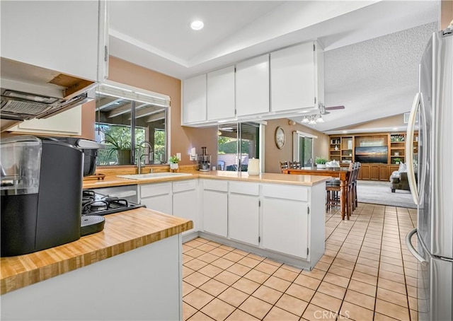 kitchen featuring white cabinetry, sink, kitchen peninsula, stainless steel fridge, and lofted ceiling