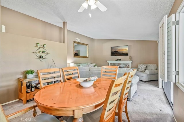 carpeted dining space featuring a textured ceiling, a stone fireplace, ceiling fan, and vaulted ceiling