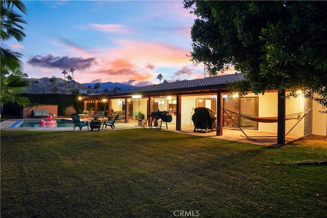 back house at dusk featuring a mountain view, a swimming pool with hot tub, a patio, and a yard