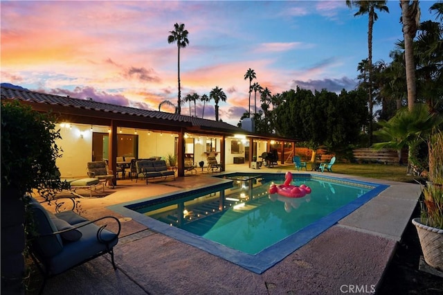 pool at dusk with a patio area, an outdoor hangout area, and a hot tub