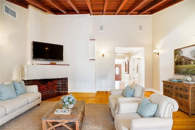 living room featuring beam ceiling, wooden ceiling, a fireplace, and light hardwood / wood-style floors