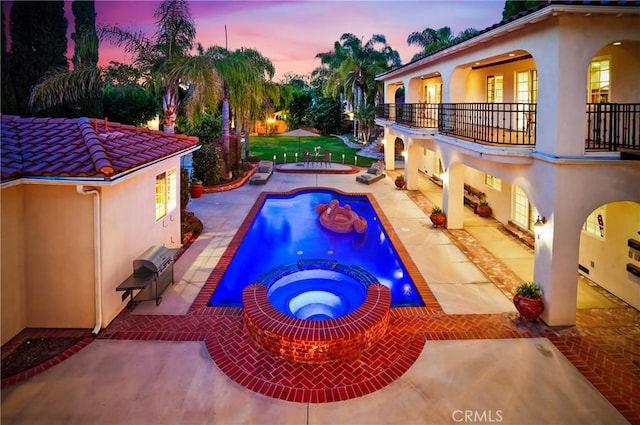 pool at dusk featuring a patio area and an in ground hot tub