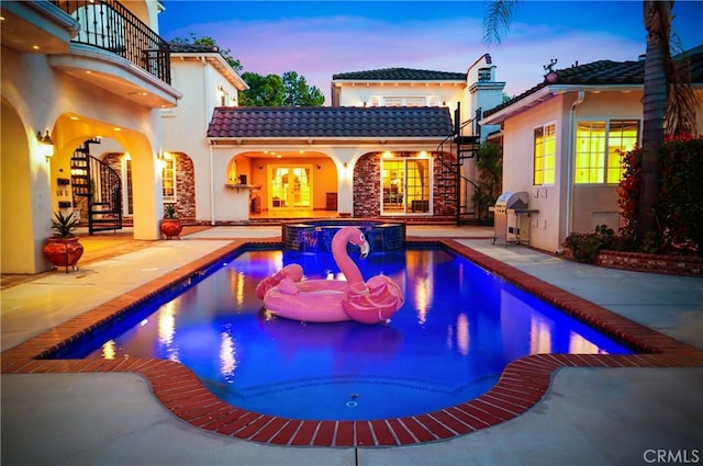 pool at dusk with an in ground hot tub, a patio, and grilling area