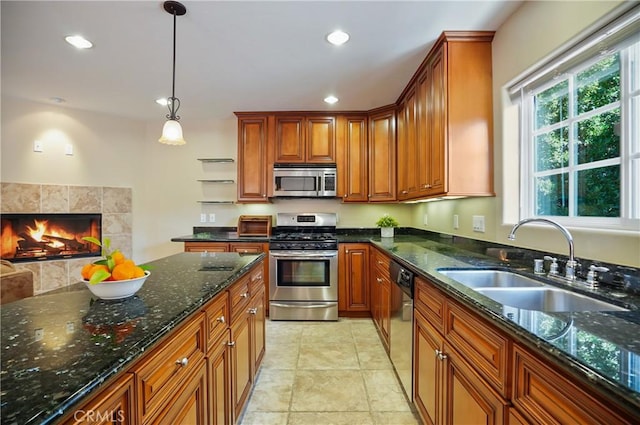 kitchen with sink, hanging light fixtures, dark stone countertops, a fireplace, and appliances with stainless steel finishes