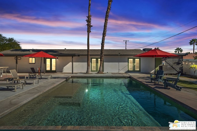 pool at dusk featuring a patio area and french doors