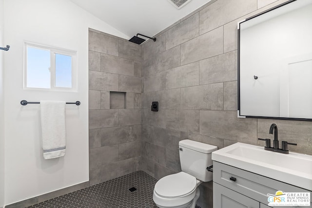 bathroom featuring a tile shower, vaulted ceiling, toilet, vanity, and tile walls