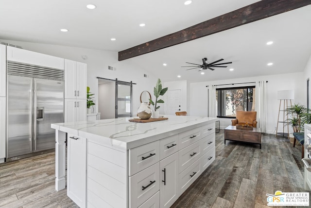 kitchen featuring a center island, vaulted ceiling with beams, a barn door, white cabinetry, and stainless steel built in refrigerator