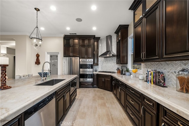 kitchen featuring sink, stainless steel appliances, wall chimney range hood, pendant lighting, and ornamental molding